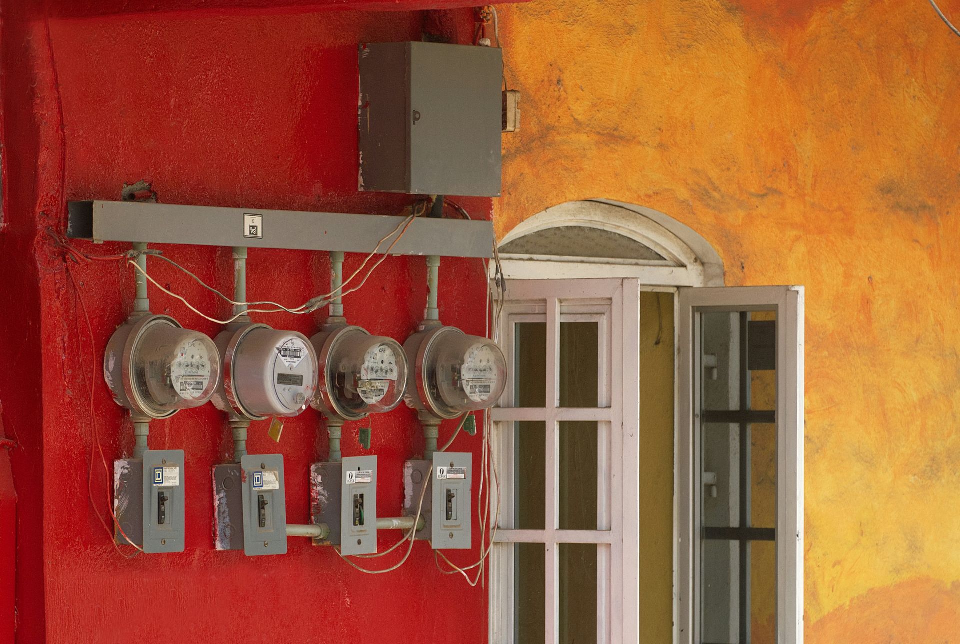 Four electric meters mounted on a red wall